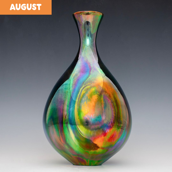Multicolored ceramic vase on a gray background with 'AUGUST' text at the top.
